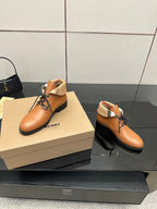 Two tan lace-up shoes on a box with black soles and plaid ankle trim