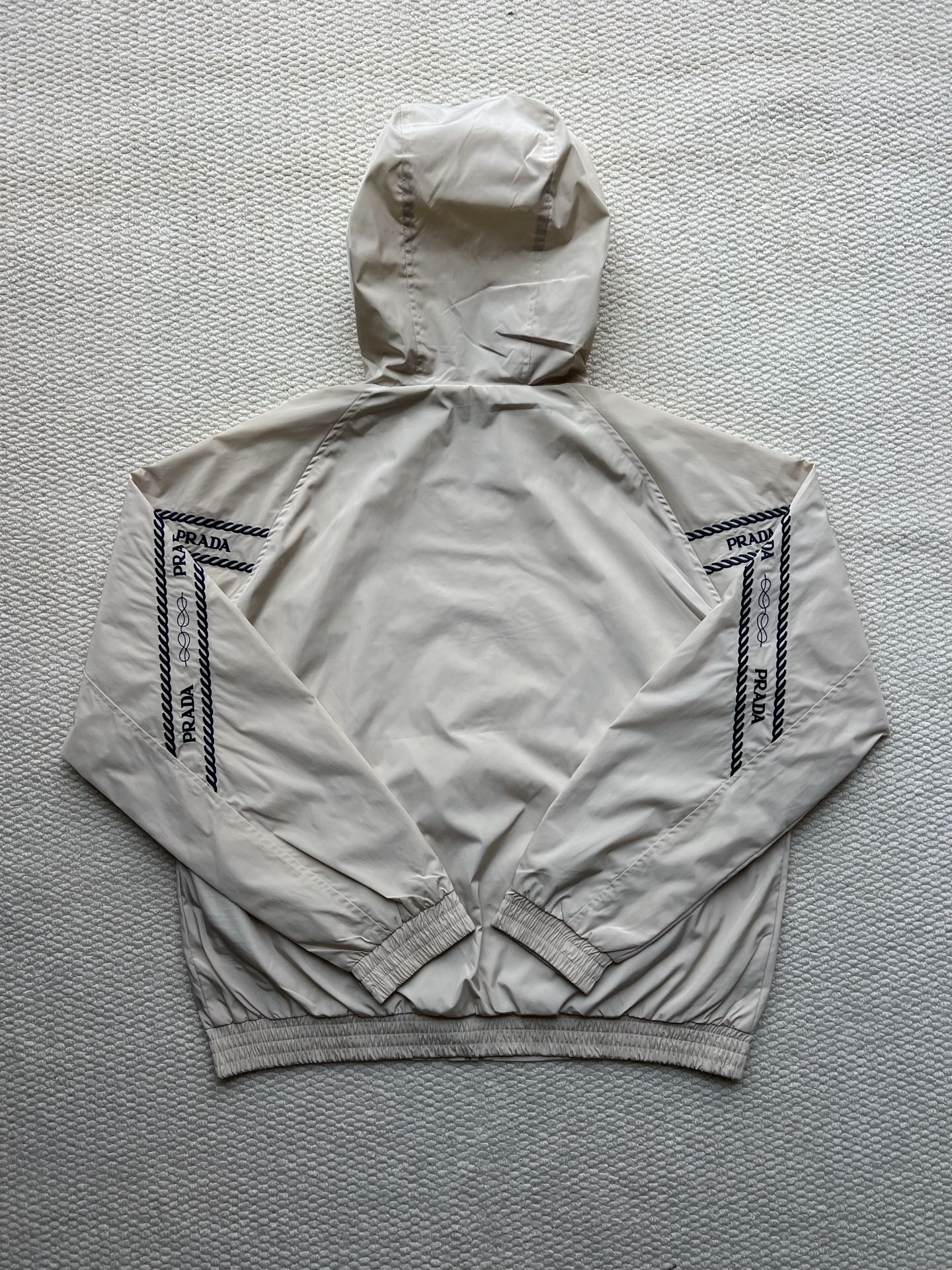Prada hooded jacket in light beige, back view with hood and logo sleeve panels.