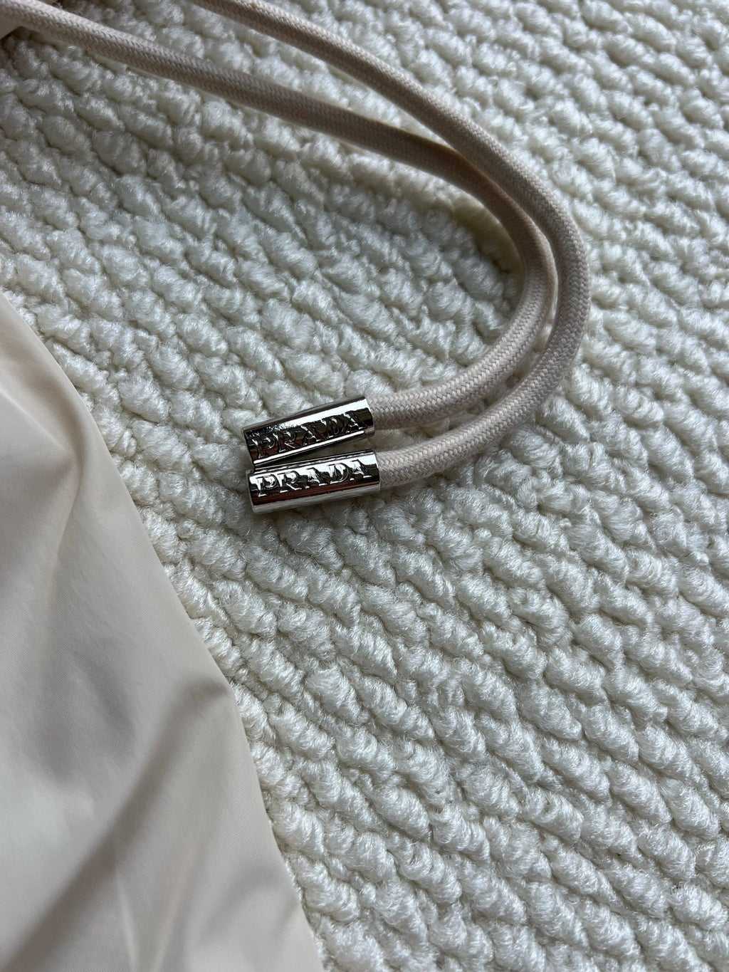 Beige hood drawstring with silver Prada logo tip on hooded jacket.
