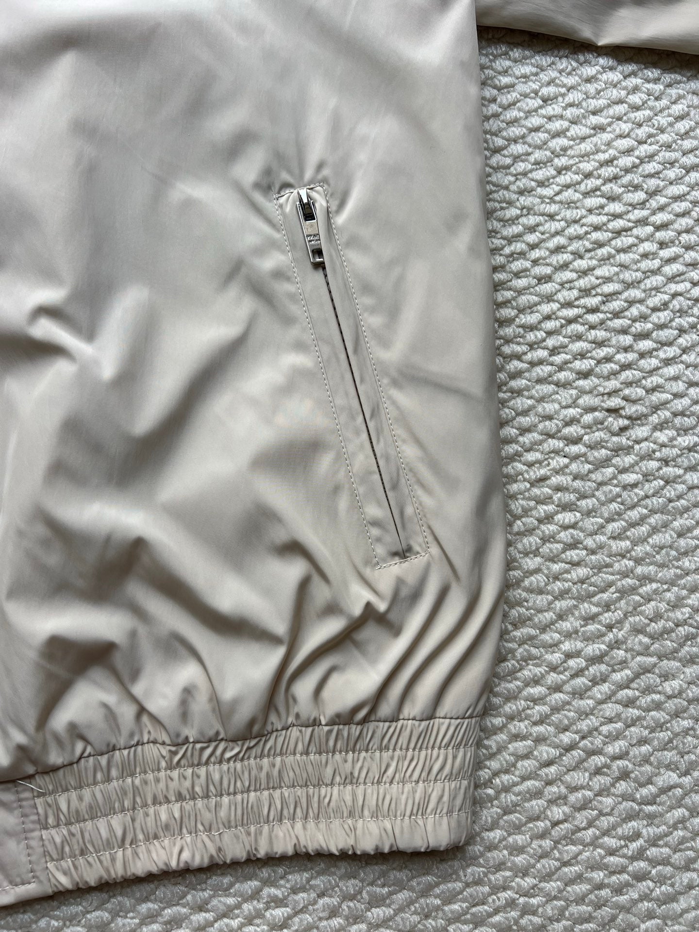 Prada hooded jacket with front zipper and ribbed elastic hem in light beige.