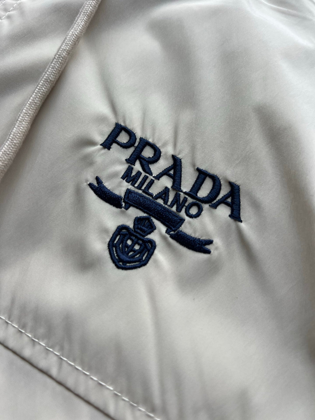 Prada Milano logo on beige hooded jacket with embroidered emblem.
