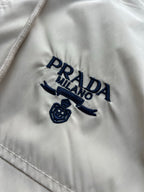 Prada Milano logo on beige hooded jacket with embroidered emblem.