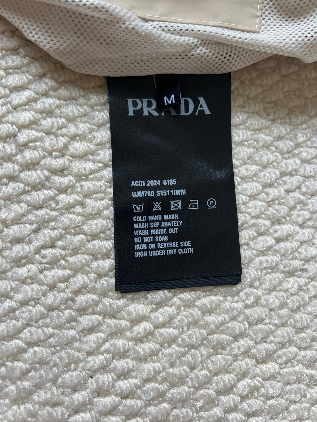 Prada care label inside jacket, black tag with white washing and warning icons.