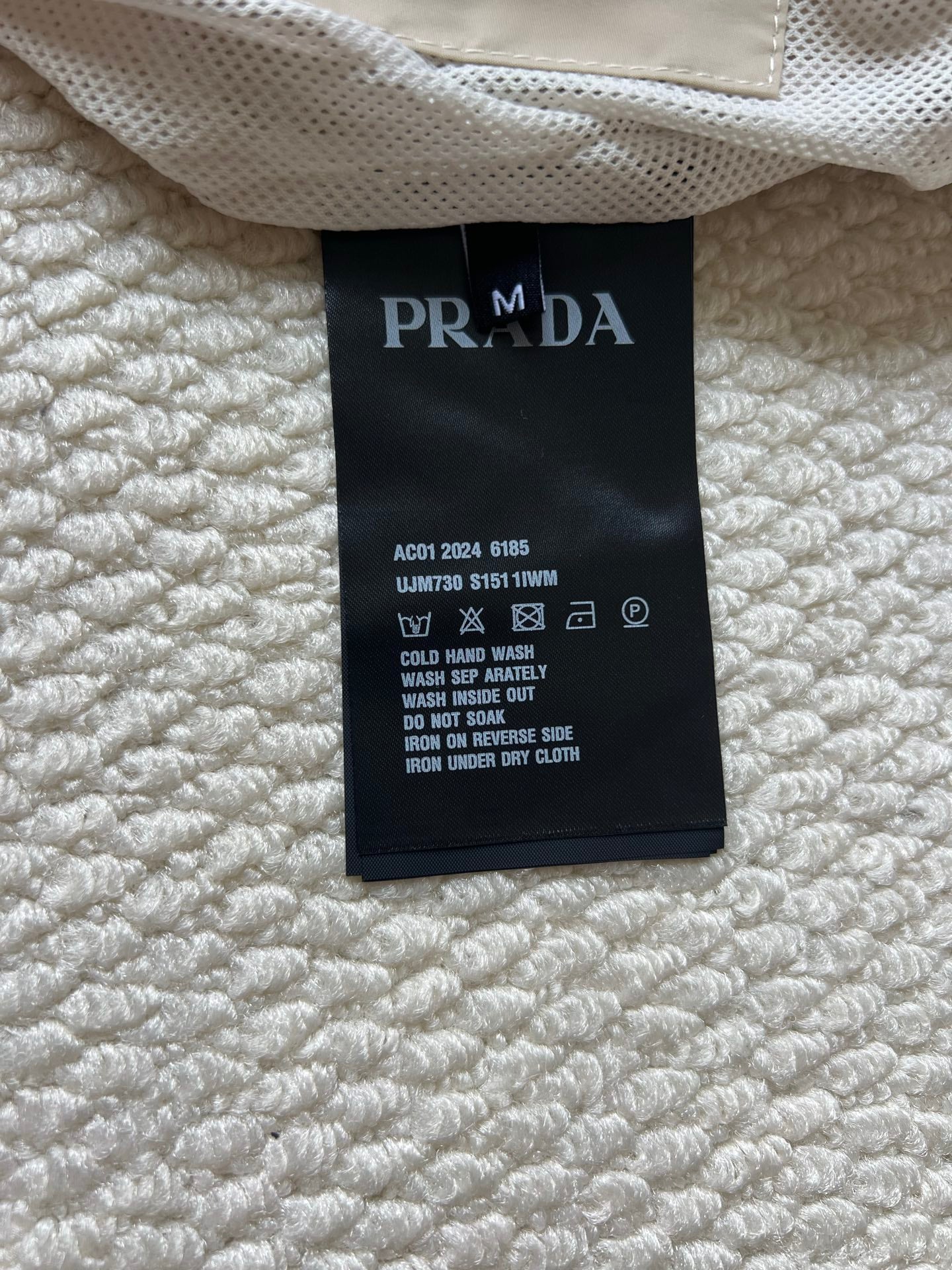 Prada care label inside jacket, black tag with white washing and warning icons.