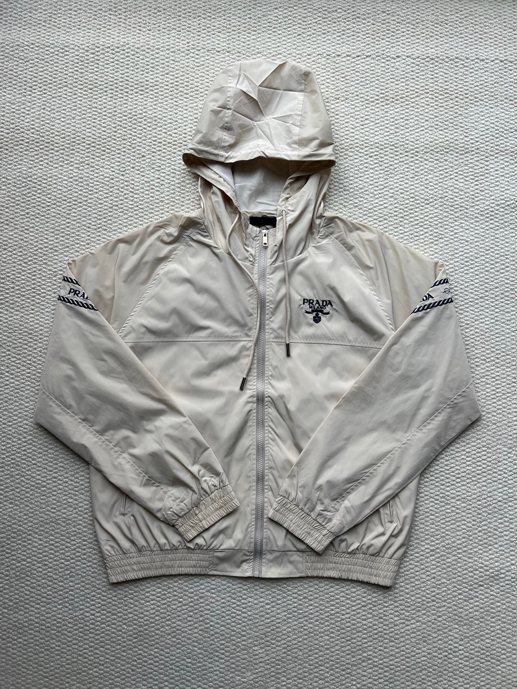 Prada hooded jacket in light beige, full zip, front logo and adjustable hood.