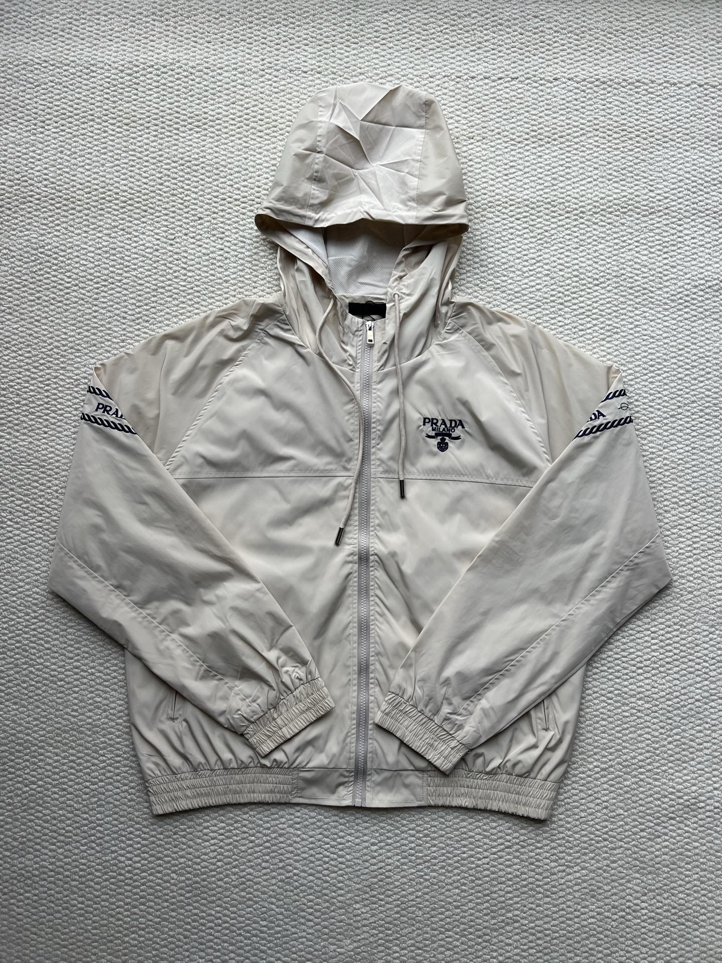 Prada hooded jacket in light beige, full zip, front logo and adjustable hood.