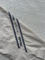 Prada hooded jacket sleeve with navy logo stripes and stitched lettering on beige.