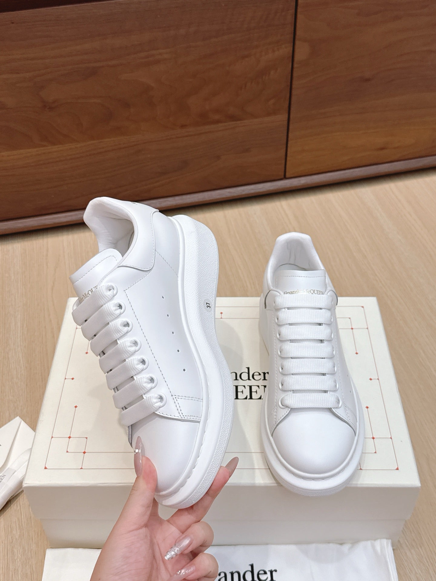 Alexander McQueen white leather sneakers, one shoe held front view, lace-up design
