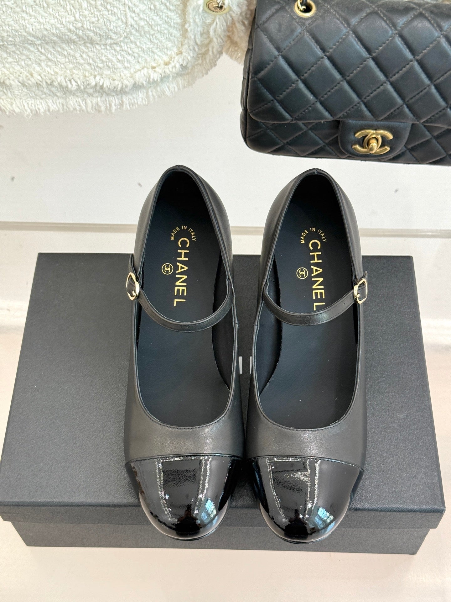 Pair of black pumps with silver patent toe caps and buckle straps, on display box