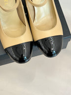 Close-up of beige Chanel flats with glossy black toe cap and bow hardware