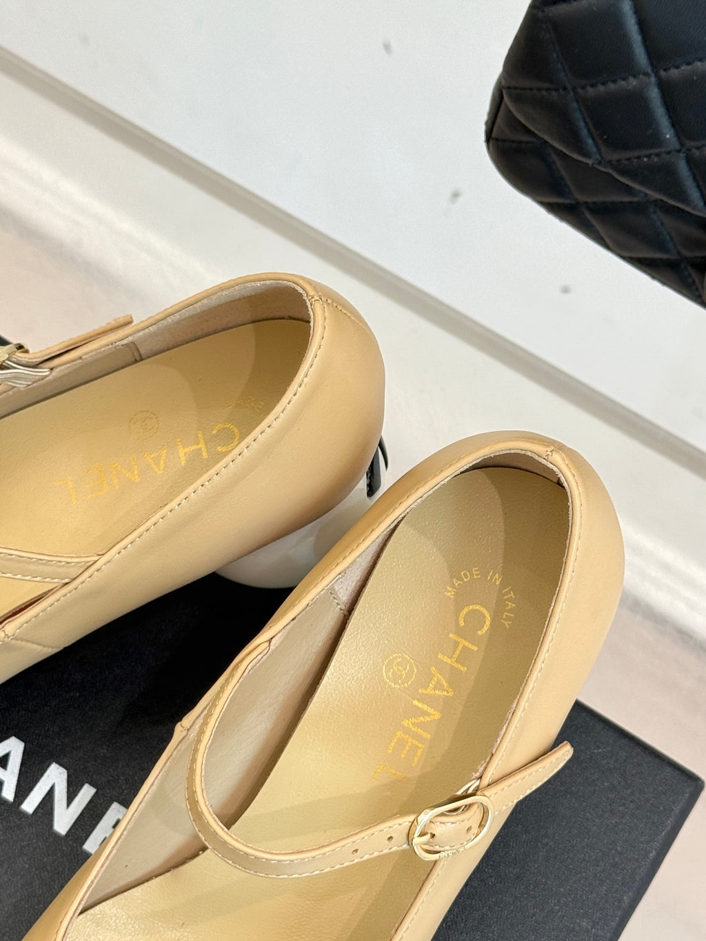 Side view of beige Chanel flats with top bow and glossy black toe cap