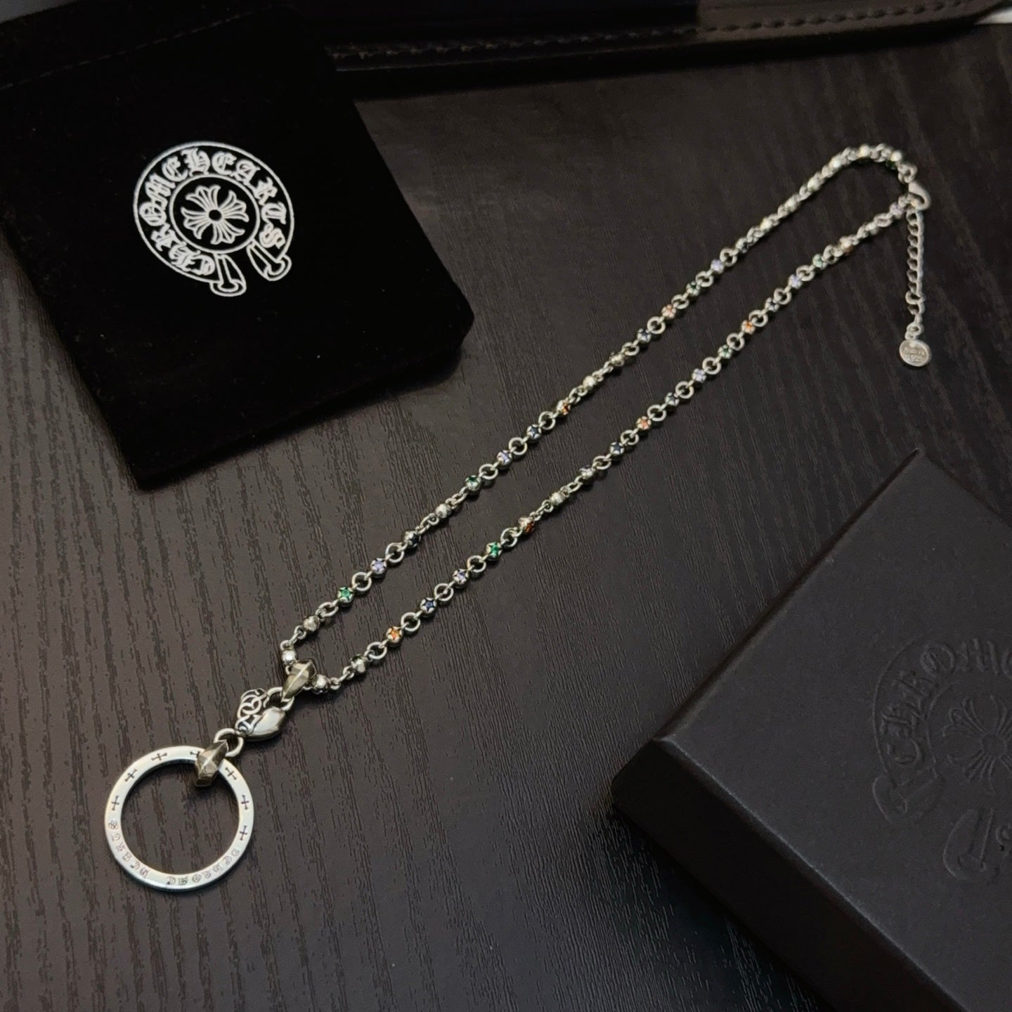 Silver-tone chain necklace with circular ring pendant next to folded jewelry box.