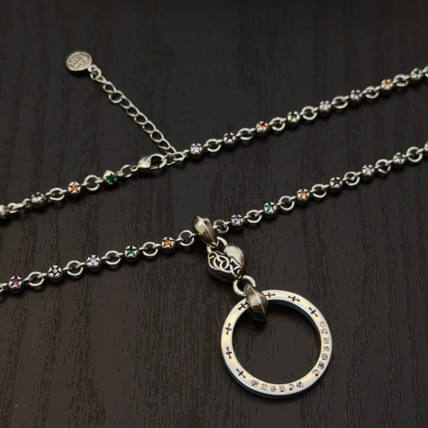 Silver-tone chain necklace with circular ring pendant; cross-studded details on links.