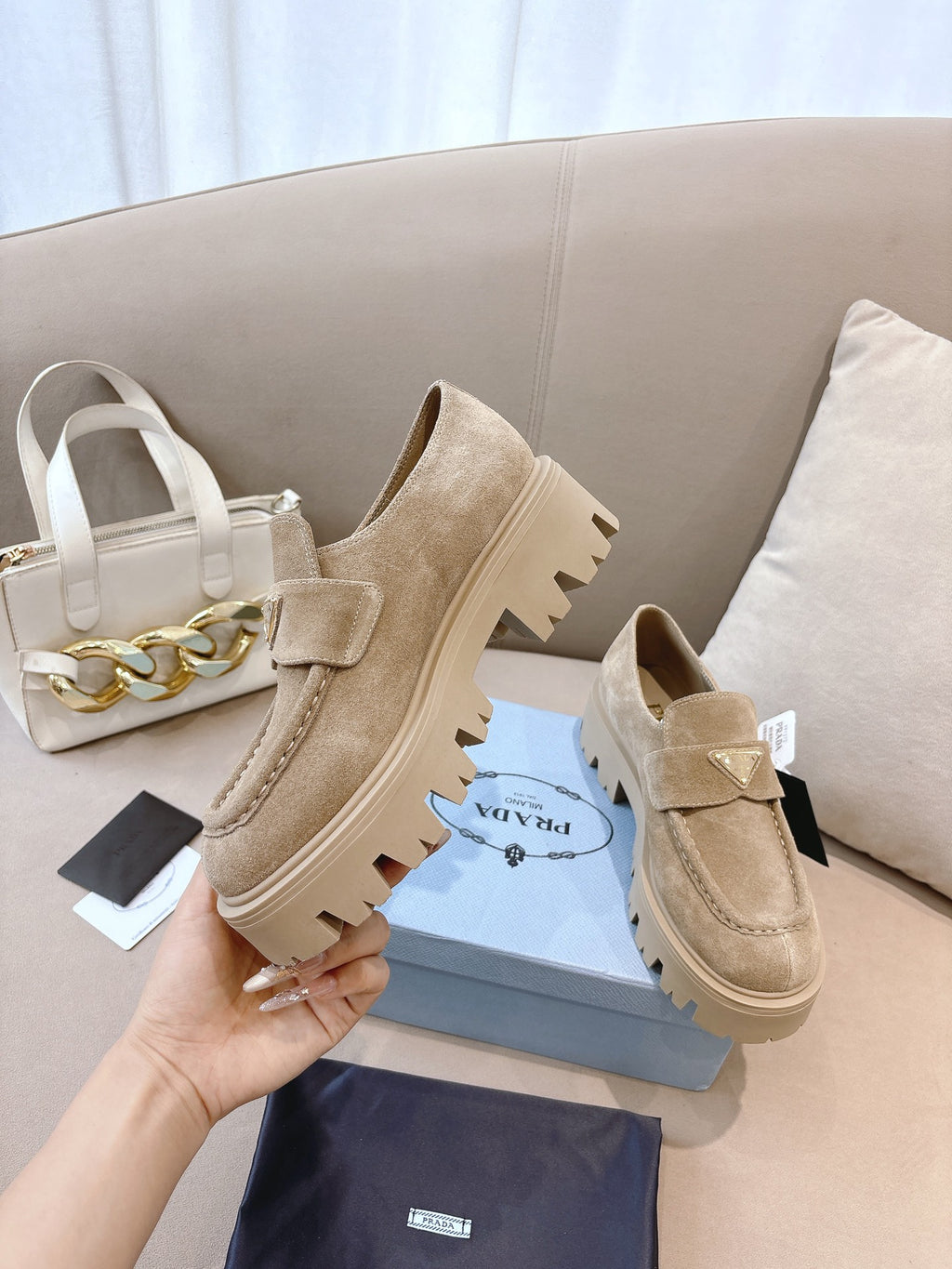 Beige suede loafer mules with strap and lug sole, Prada held in hand