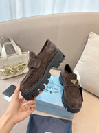 Dark brown suede loafers on blue box, chunky lug outsole and strap with logo