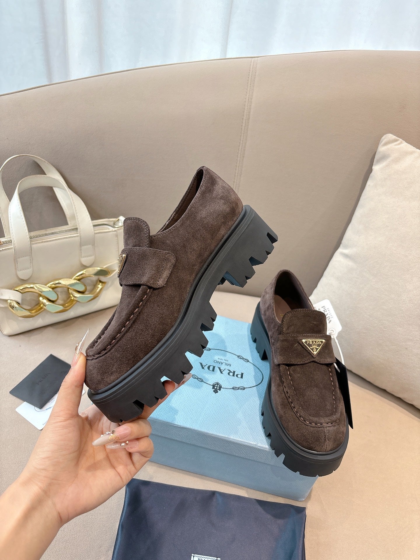 Dark brown suede loafers on blue box, chunky lug outsole and strap with logo