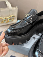 Close-up Prada black patent loafer with buckle strap, glossy finish, and platform tread