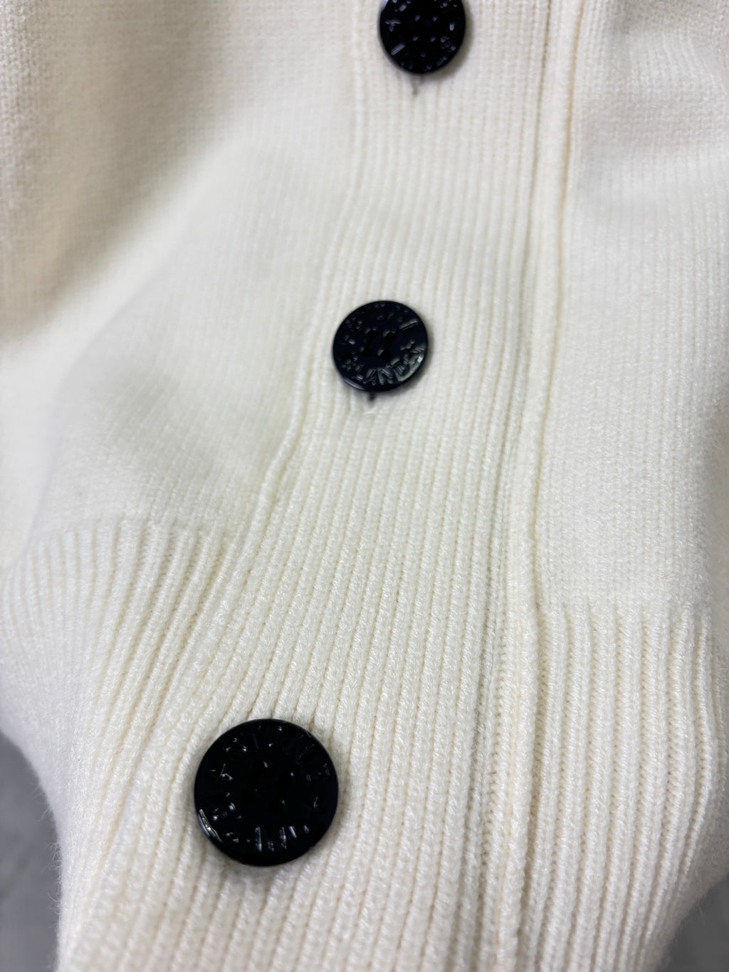 Cream knit cardigan front with black button detail and textured ribbed placket