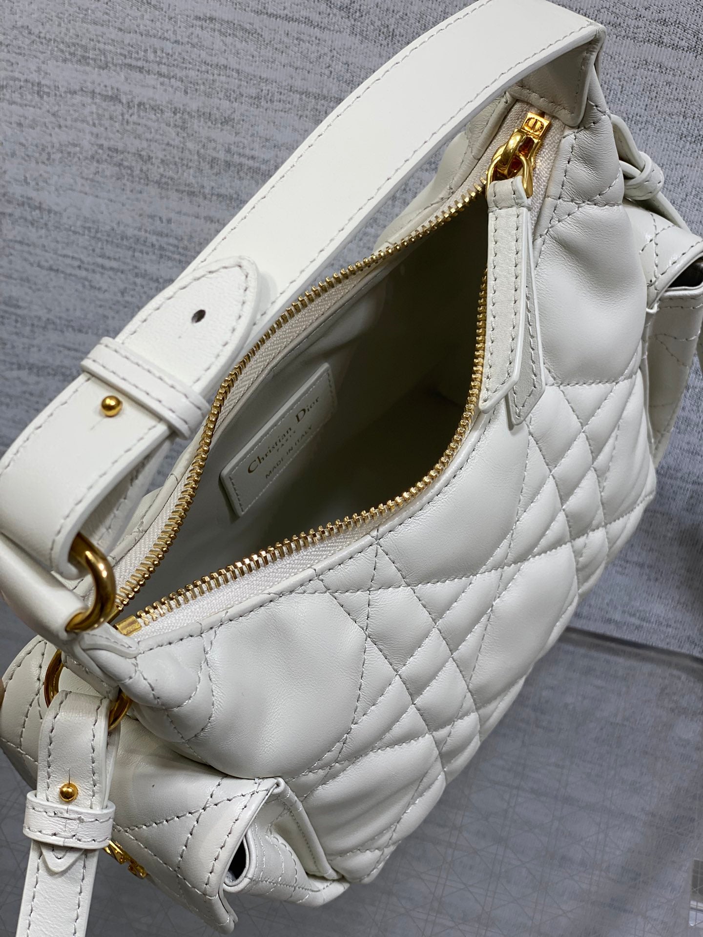 White Dior quilted crossbody bag showing gold zipper, interior pocket, and strap D-ring.