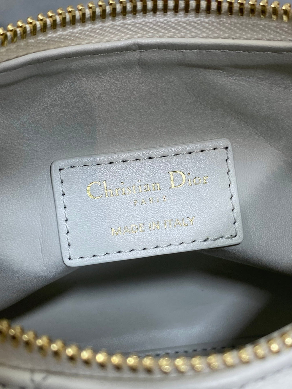 Dior label inside white quilted bag, stitched text with gold zipper edge.