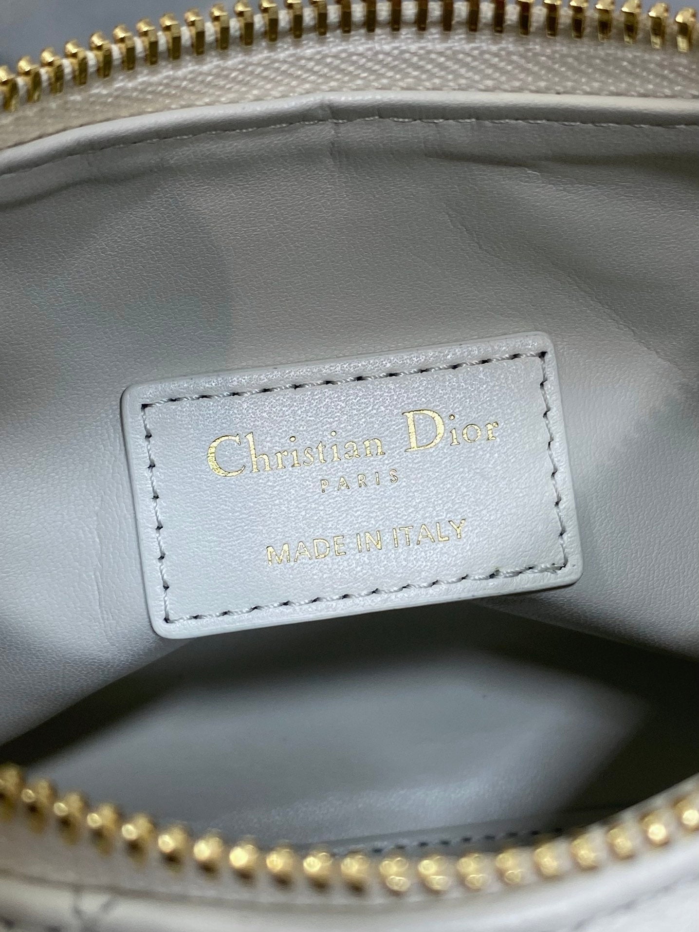 Dior label inside white quilted bag, stitched text with gold zipper edge.