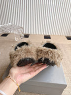 Balenciaga beige furry slide sandals held in hand, showing black interior soles
