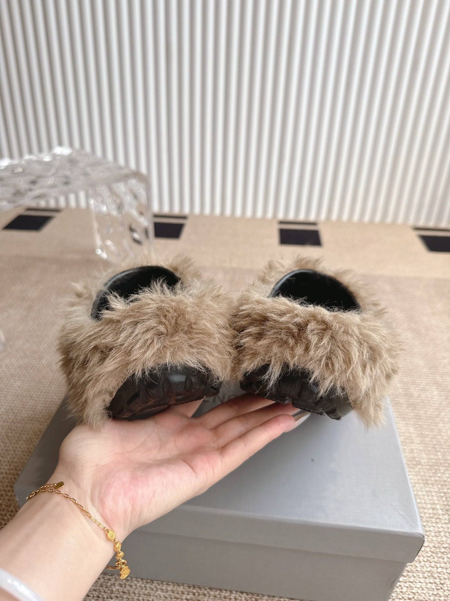 Balenciaga beige furry slide sandals held in hand, showing black interior soles