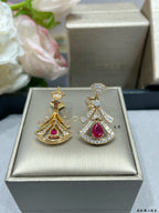 Two dangling earrings in box: one gold-tone and one silver-tone, both with red teardrops.