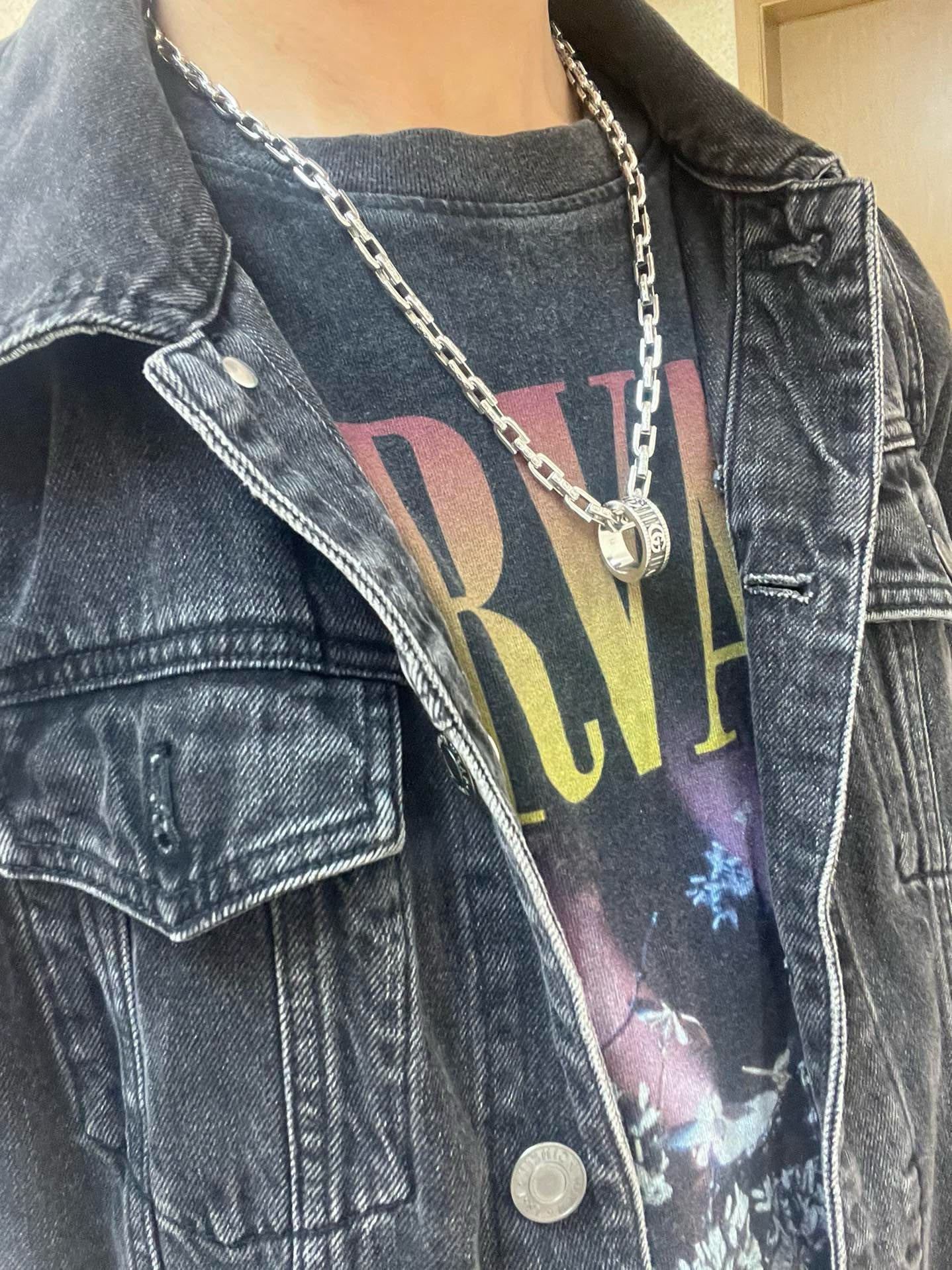 Silver-tone chain necklace with small circular logo pendant on denim jacket