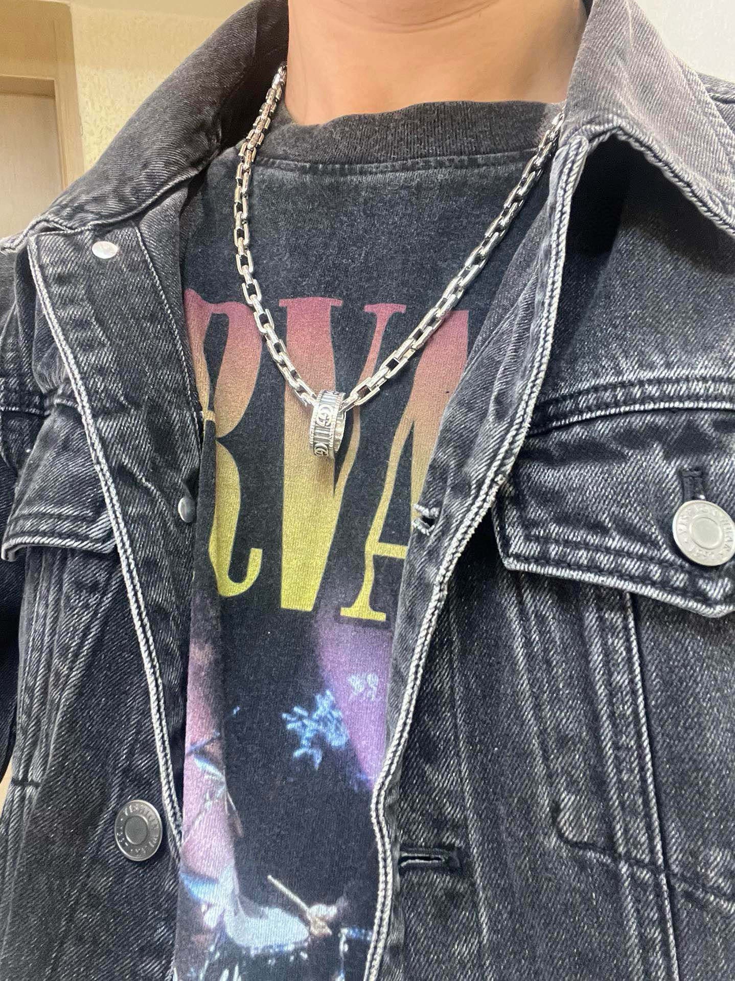 Silver-tone chain necklace with small pendant on denim jacket and graphic T-shirt