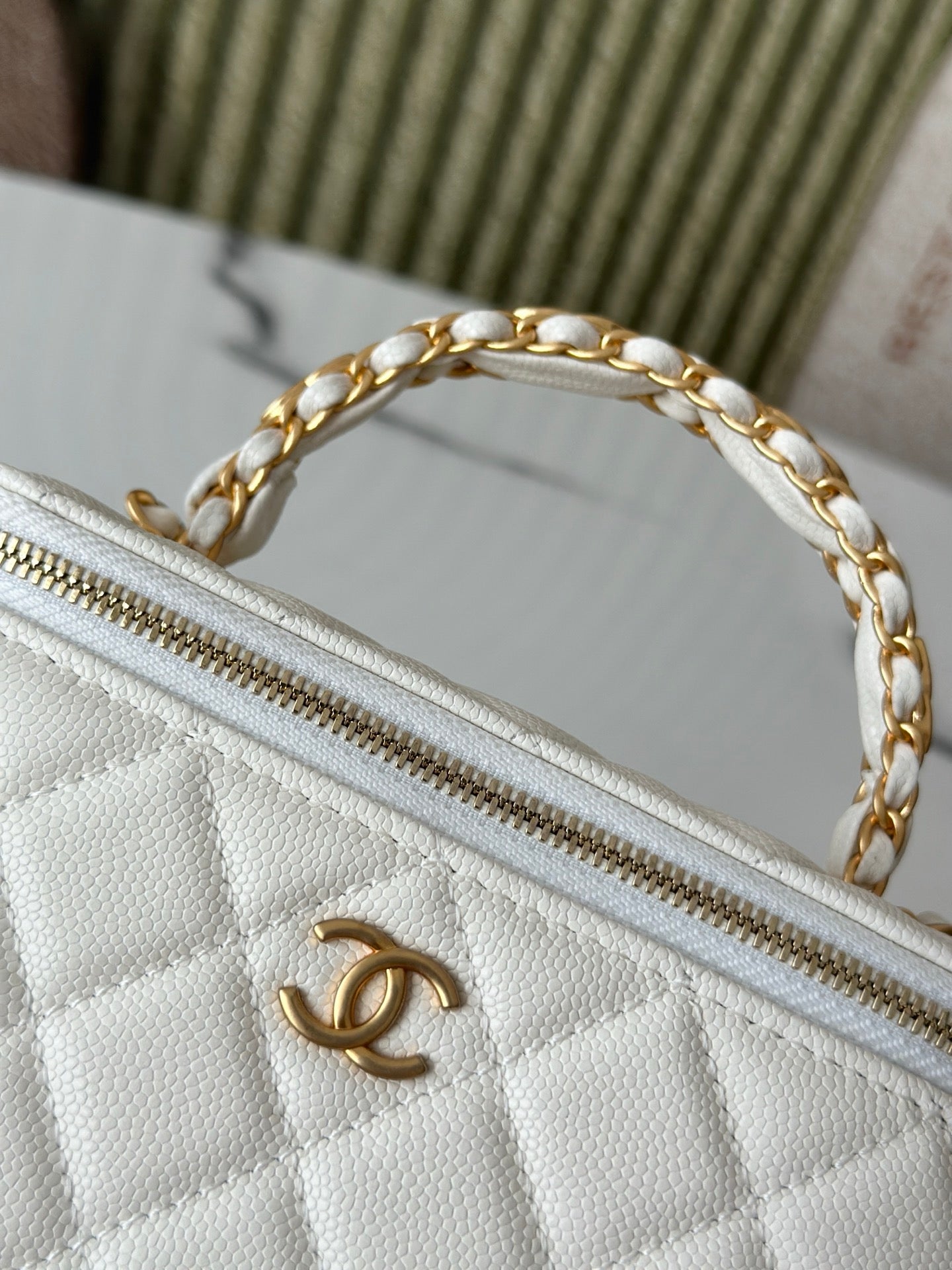 White quilted mini handbag close-up of gold zipper and chain strap ring.
