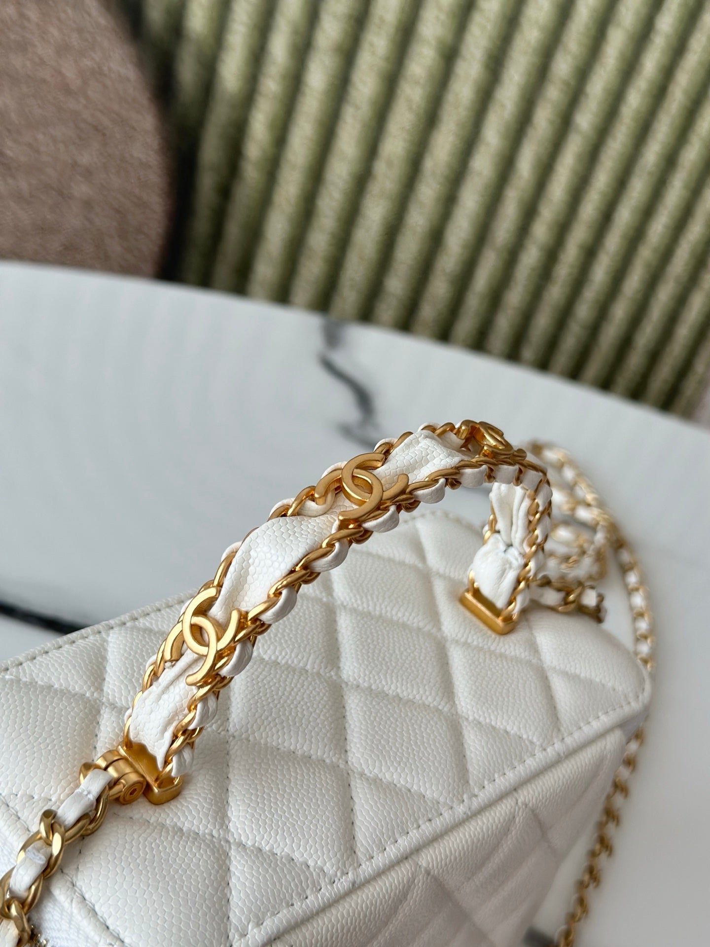 White quilted mini handbag close-up with gold chain, handle and flap details.