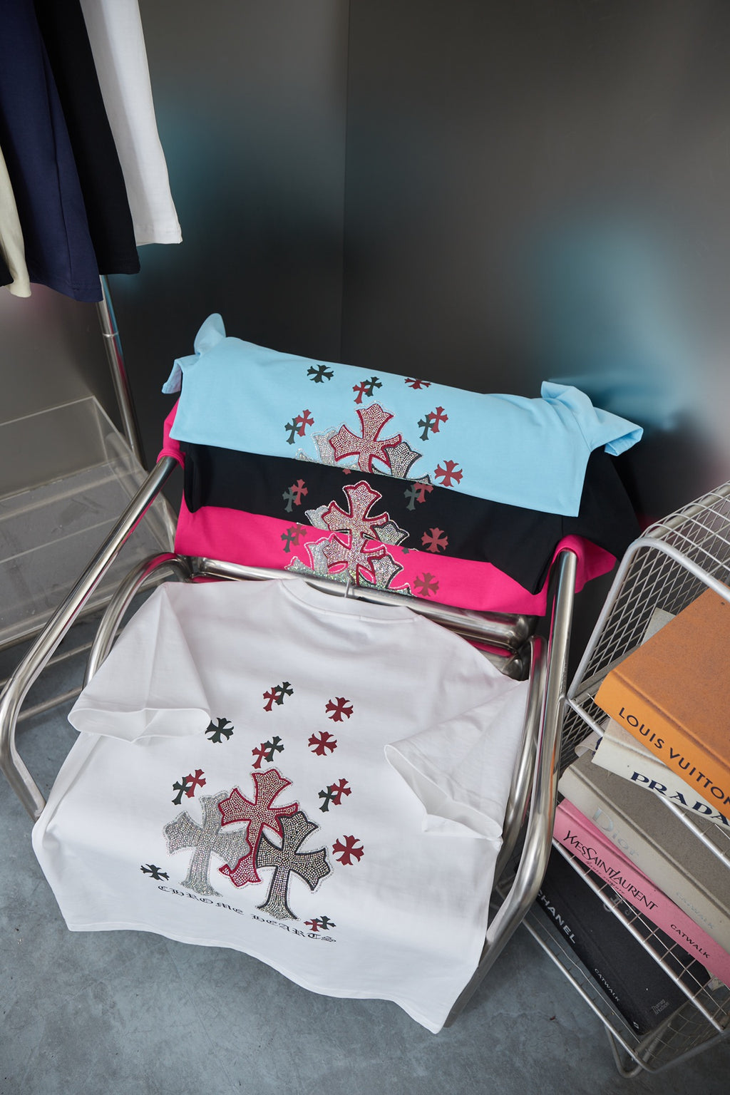 Folded T-shirts in white, black, and light blue with red-and-black cross prints