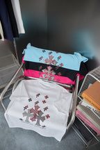 Folded T-shirts in white, black, and light blue with red-and-black cross prints