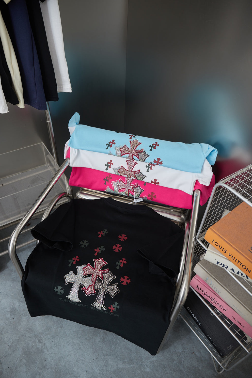 Folded T-shirts in white, blue, and pink with red cross emblems on hanger