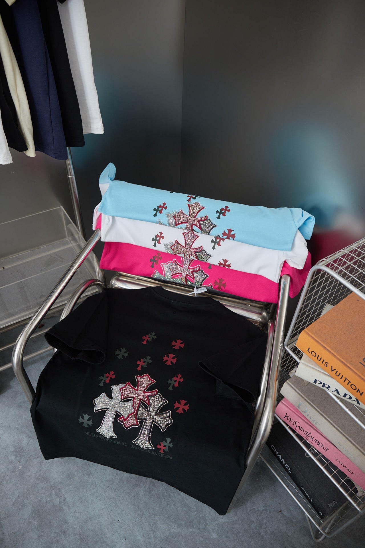 Folded T-shirts in white, blue, and pink with red cross emblems on hanger