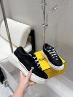Black Fendi sneakers held in hand, white platform sole, lace-up and logo heel tabs.