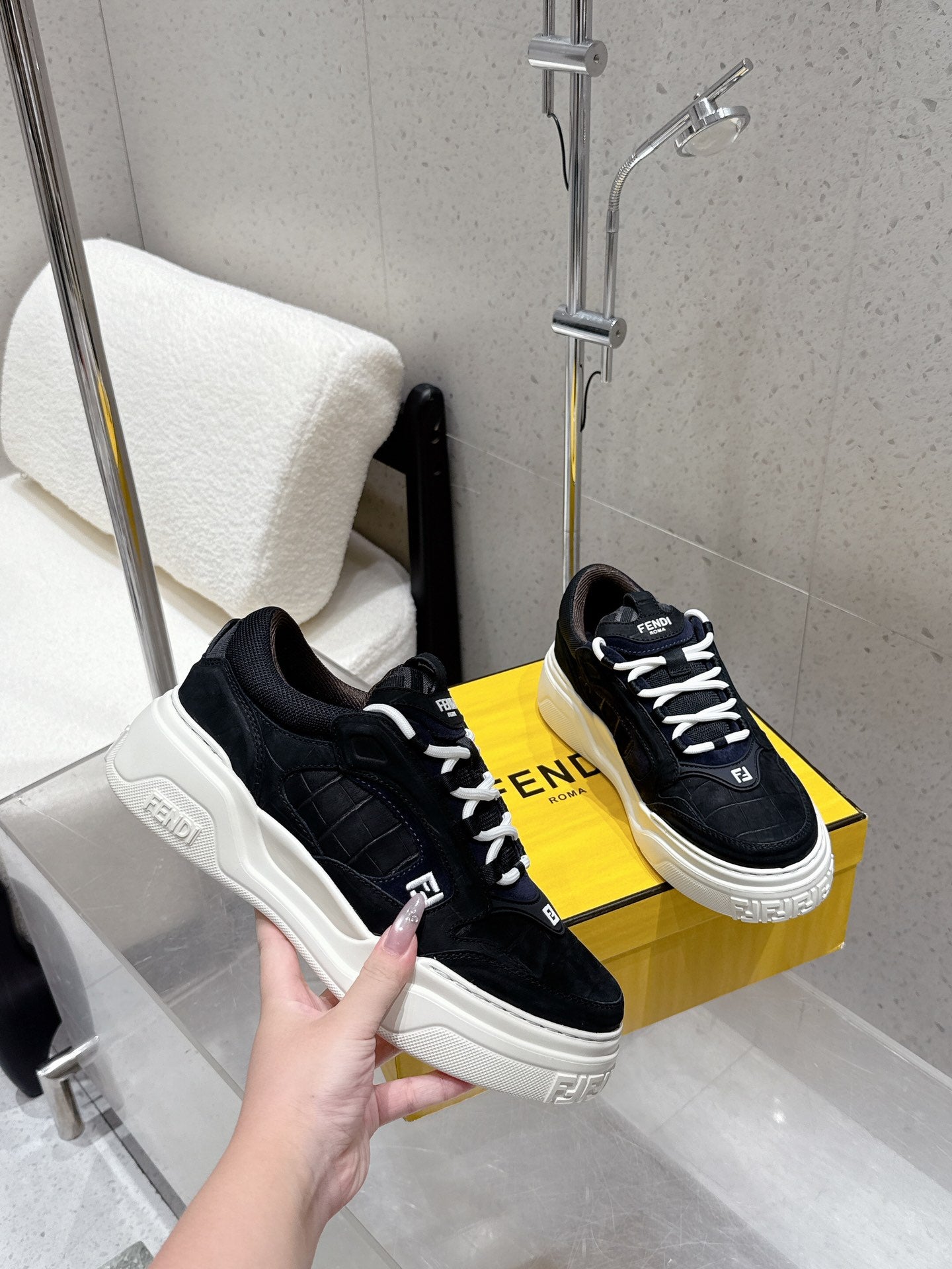 Black Fendi sneakers held in hand, white platform sole, lace-up and logo heel tabs.