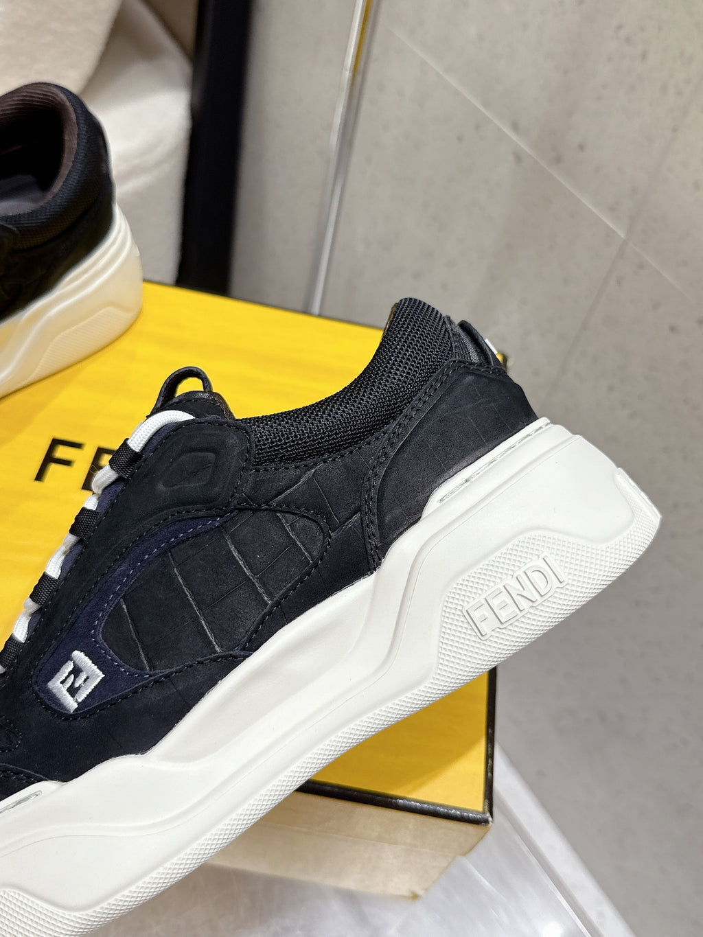 Black Fendi sneakers close-up, dark blue suede overlays, white sole and F logo patch.