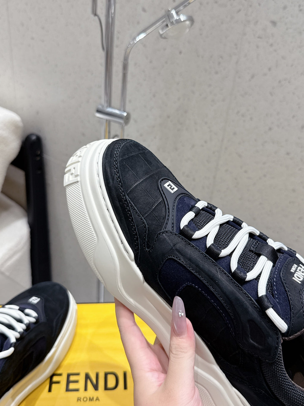 Black Fendi sneaker close-up, white laces, textured upper and stitched side panel.