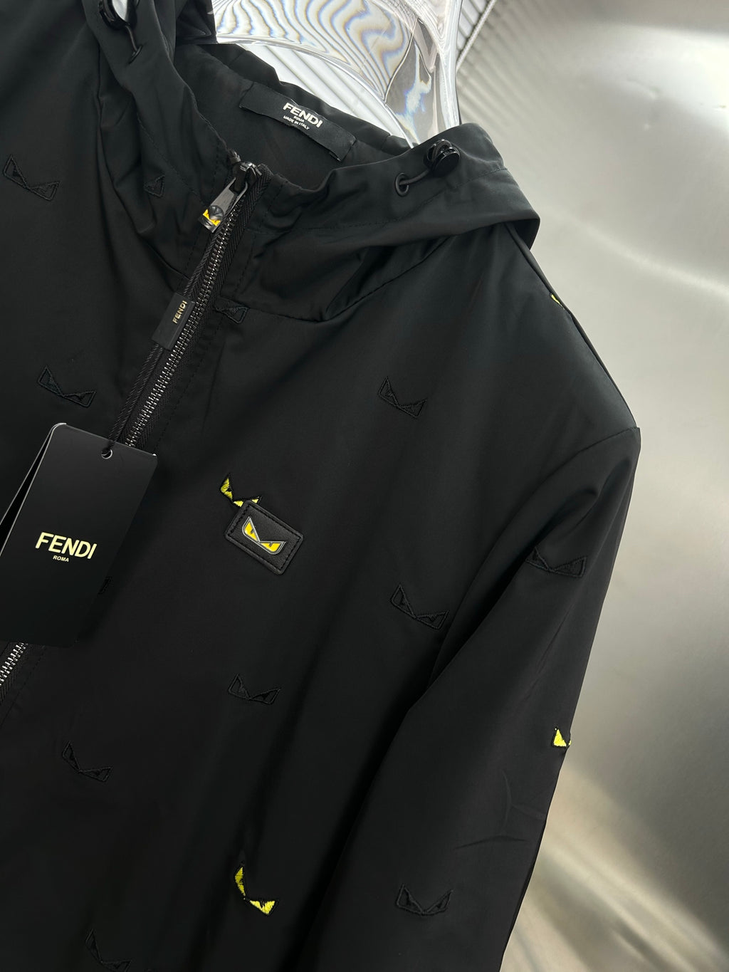Long jacket close-up: black chest panel with logo patch, front zipper, yellow prints