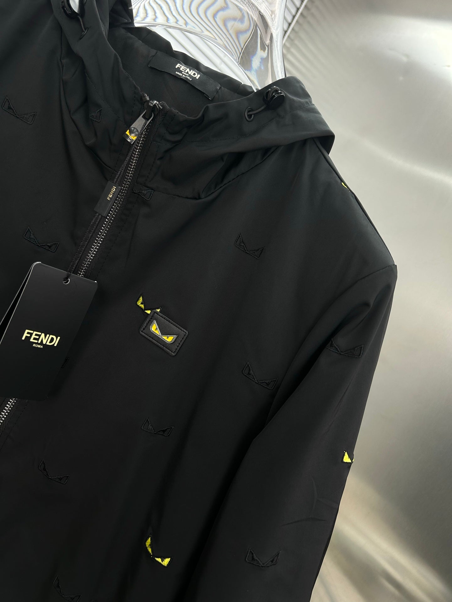 Long jacket close-up: black chest panel with logo patch, front zipper, yellow prints