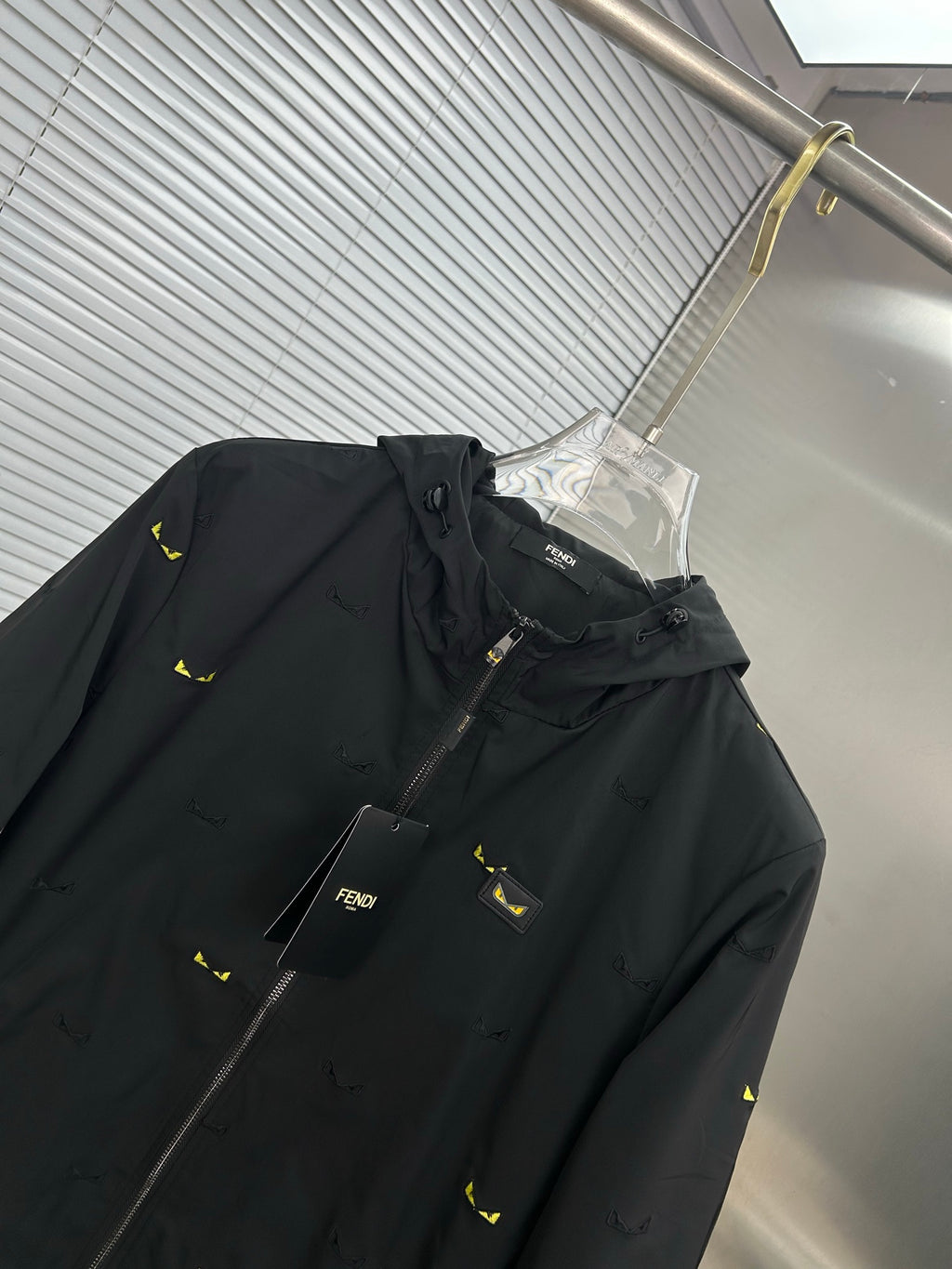Long jacket close-up: black hood with drawstring, front zipper, yellow mini print