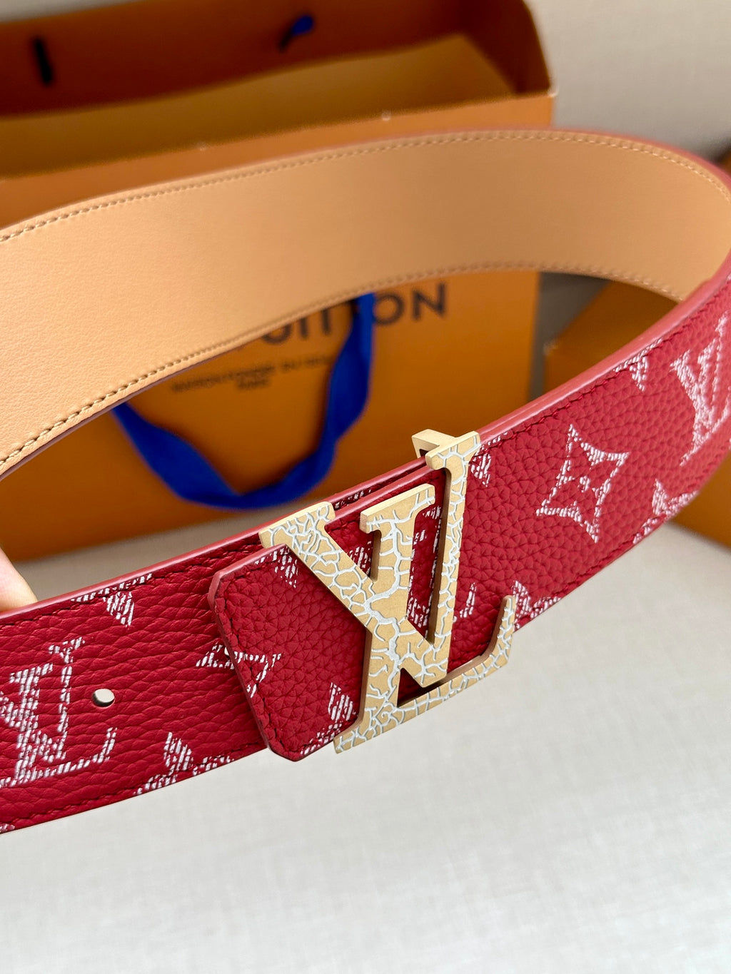 Louis Vuitton belt buckle detail on red monogram strap