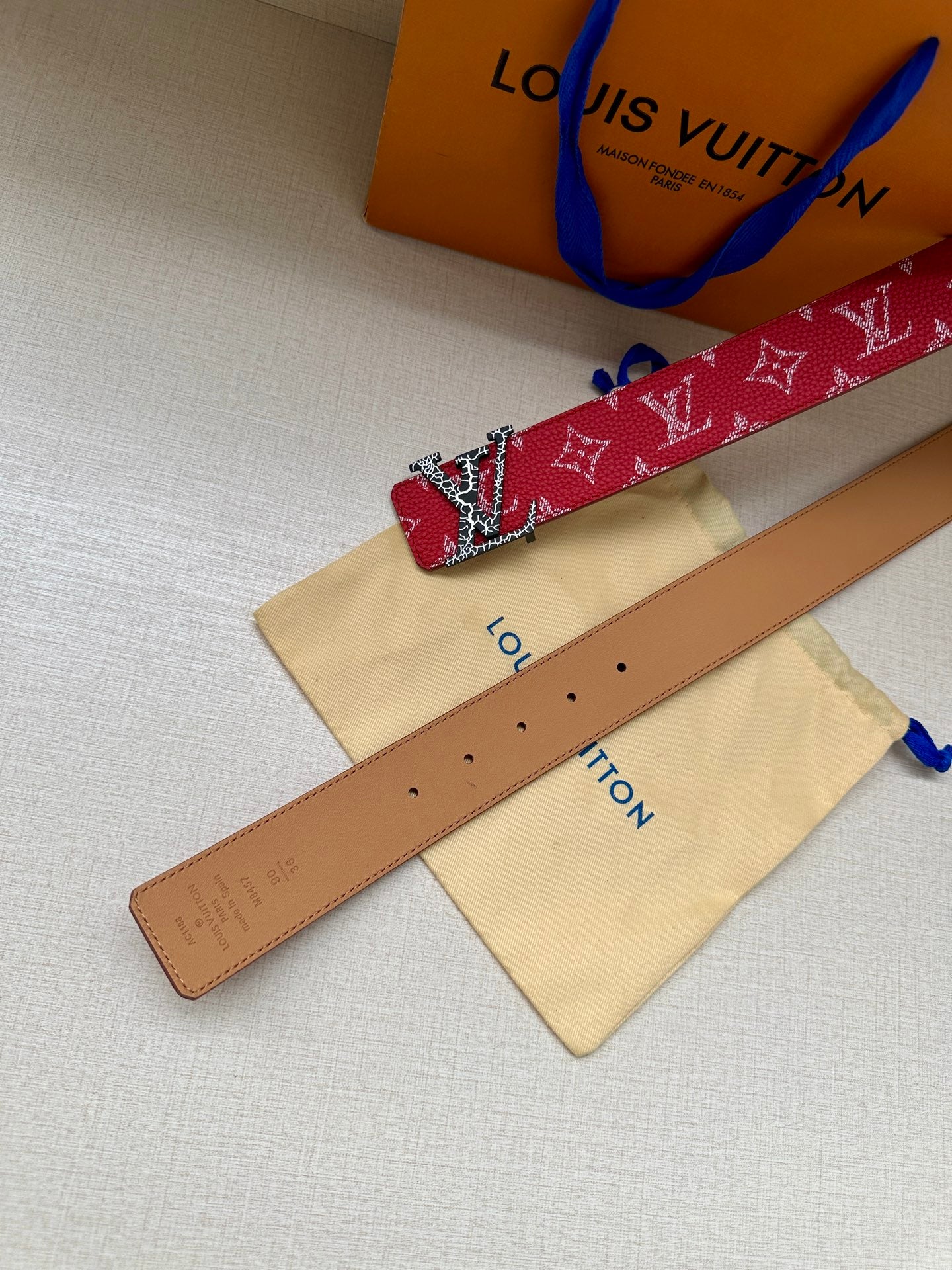 Louis Vuitton belt with red monogram strap, gold buckle, and punched holes