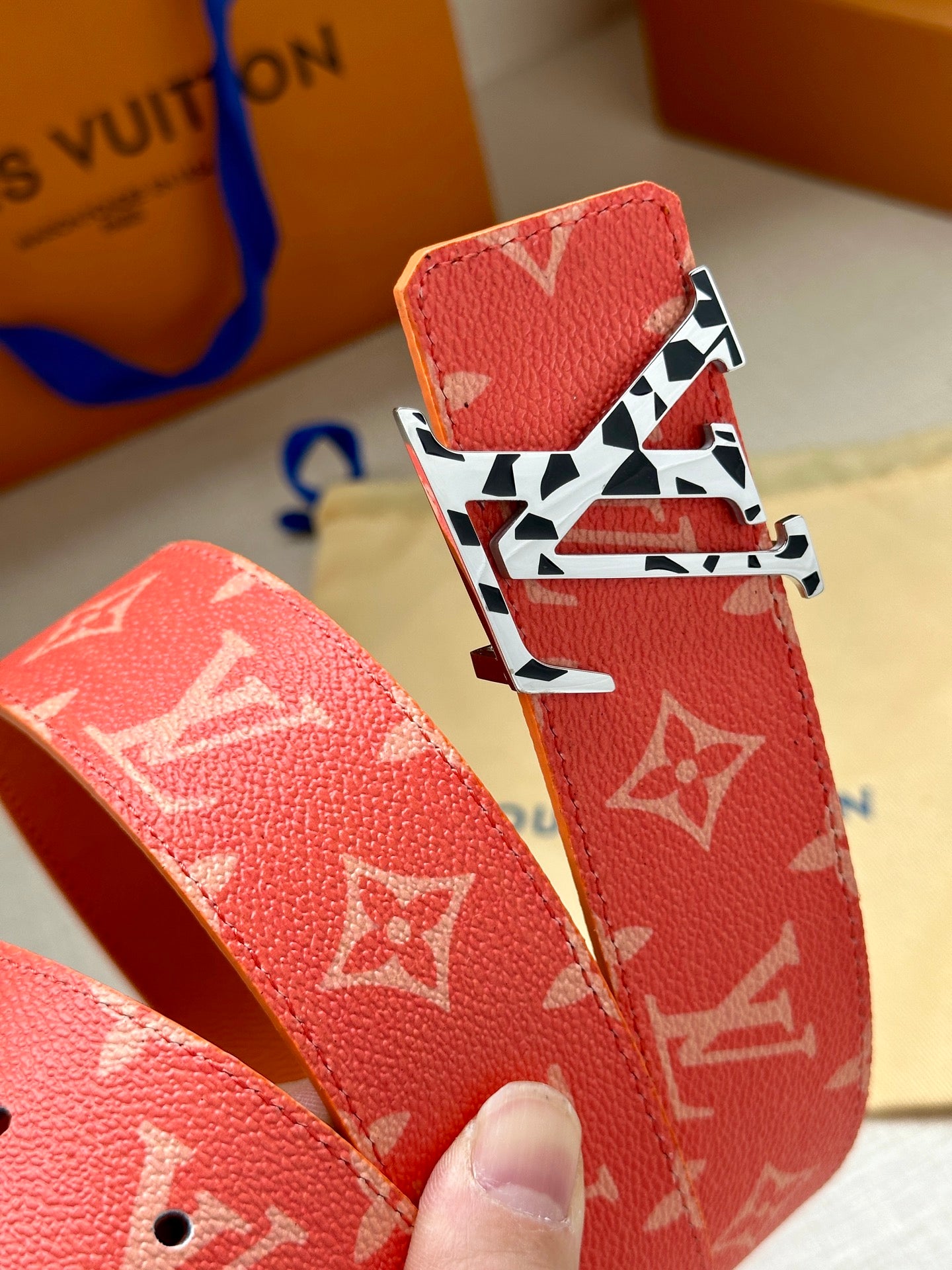 Red monogram belt end with punched holes and textured leather, metal buckle close-up.