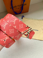 Red monogram belt close-up of metal buckle and patterned strap end with punched holes.
