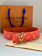 Red monogram belt with metal buckle and perforated strap holes on a light fabric surface.