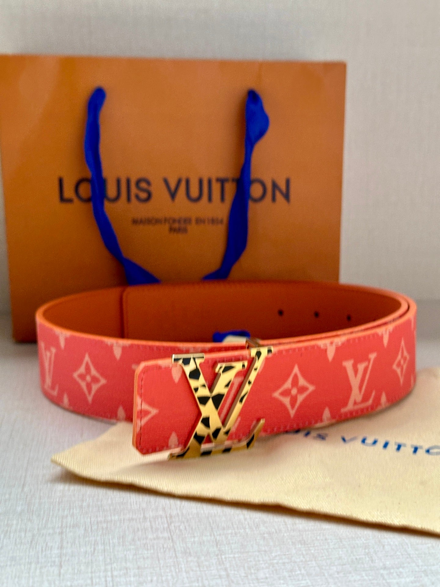 Red monogram belt with metal buckle and perforated strap holes on a light fabric surface.
