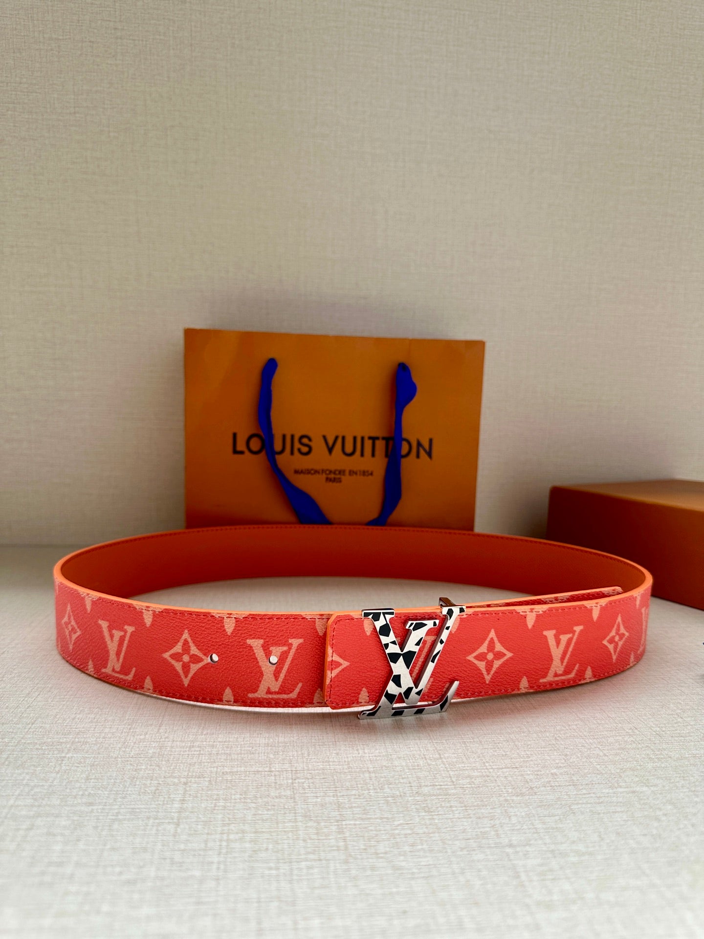 Red monogram belt with metal buckle, adjustable holes, and logo pattern all over.